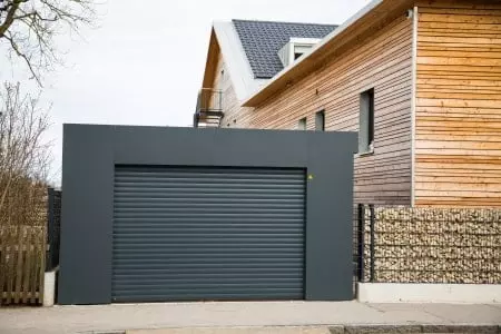 Schwarze Garage mit schwarzem Garagentor neben einem Holzhaus.