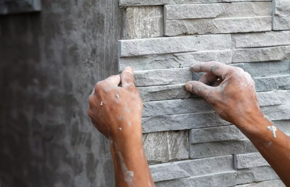 Person platziert grauen Naturstein in einer Natursteinwand.